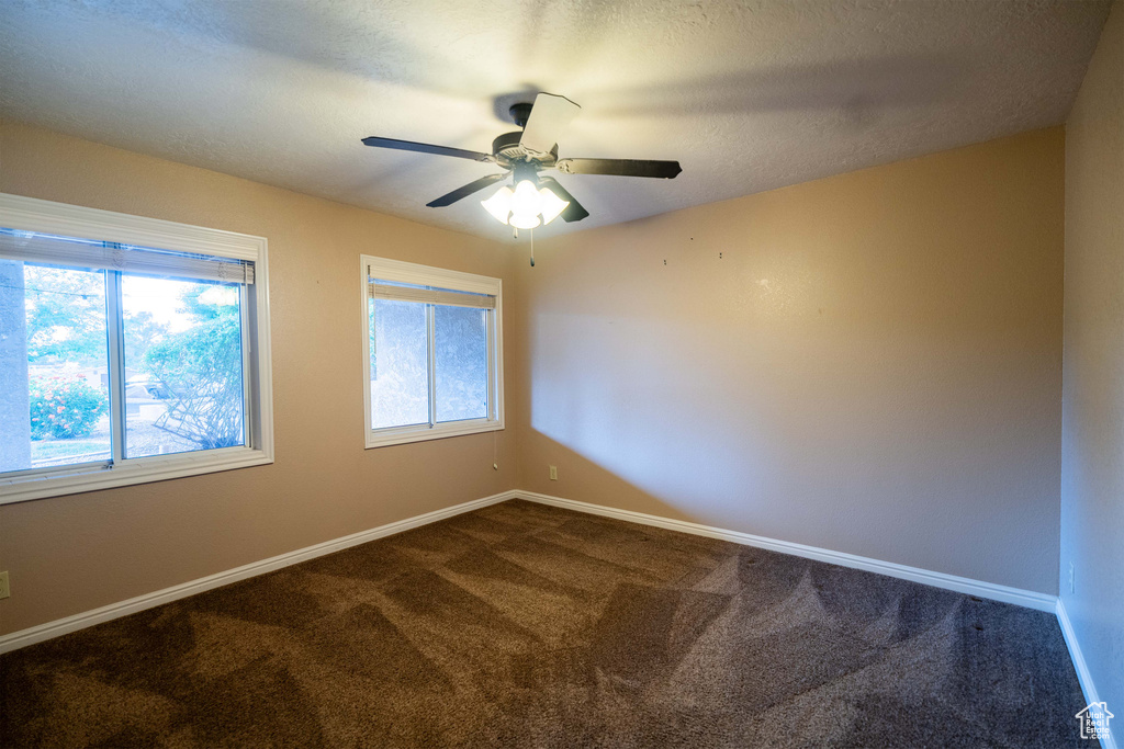 Spare room featuring dark colored carpet, baseboards, and ceiling fan