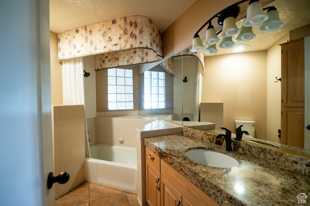 Bathroom featuring a garden tub, tile patterned flooring, a textured ceiling, toilet, and vanity