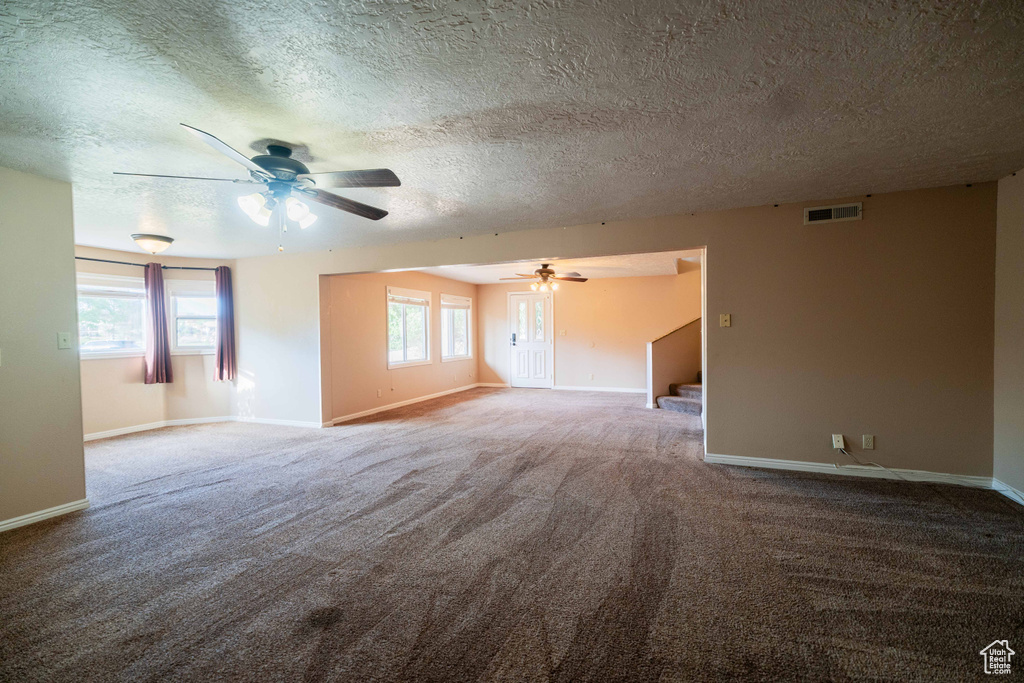 Carpeted spare room with a ceiling fan, baseboards, a textured ceiling, and stairs