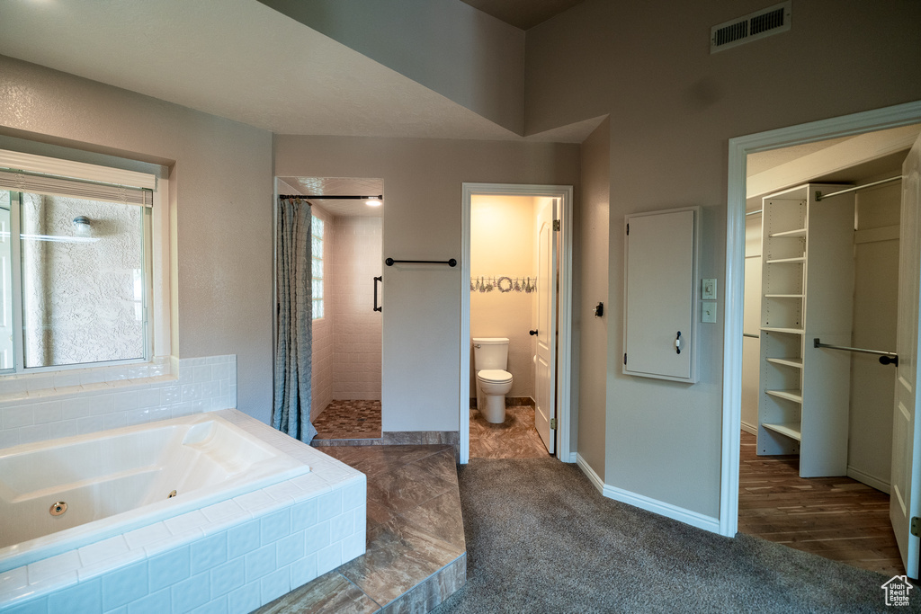 Bathroom featuring tiled shower, a jetted tub, toilet, a walk in closet, and baseboards