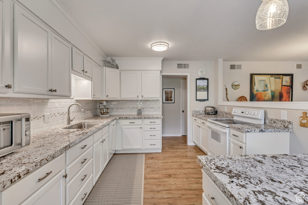 Kitchen with white electric stove, a sink, light wood-type flooring, white cabinets, and decorative backsplash