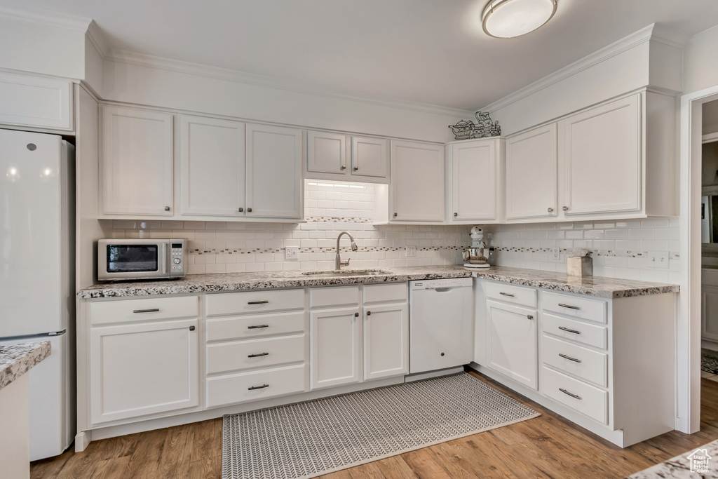 Kitchen featuring white appliances, a sink, white cabinetry, and crown molding