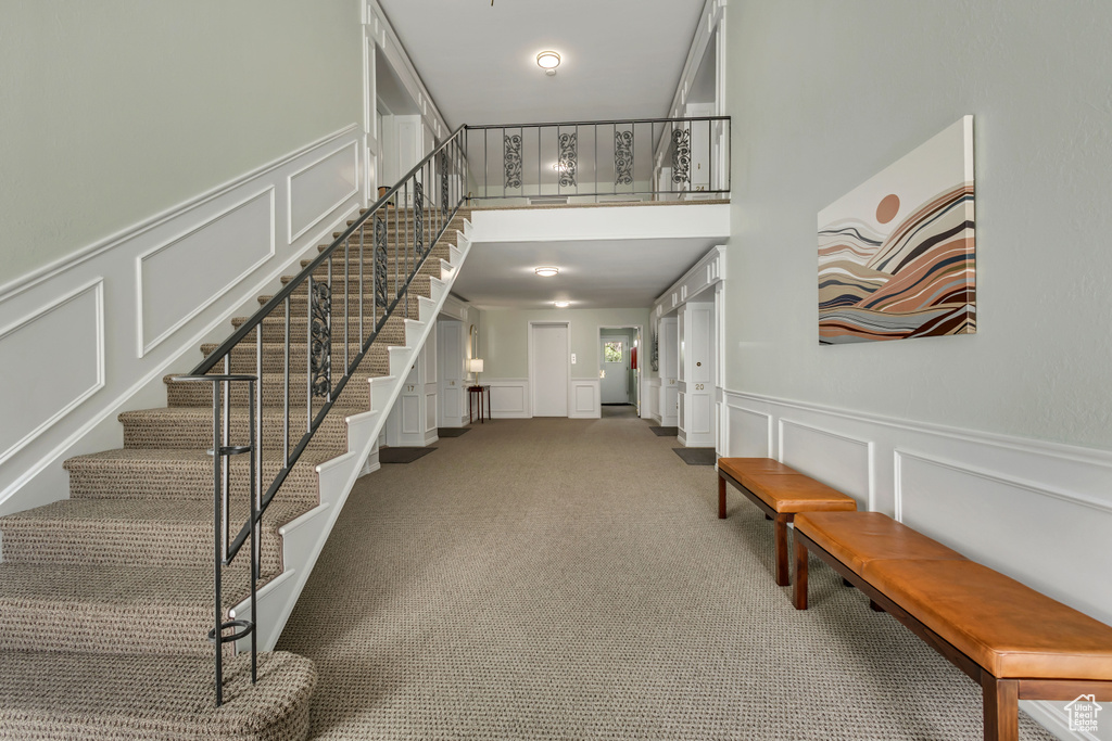 Entryway with a decorative wall, stairs, carpet floors, and a wainscoted wall