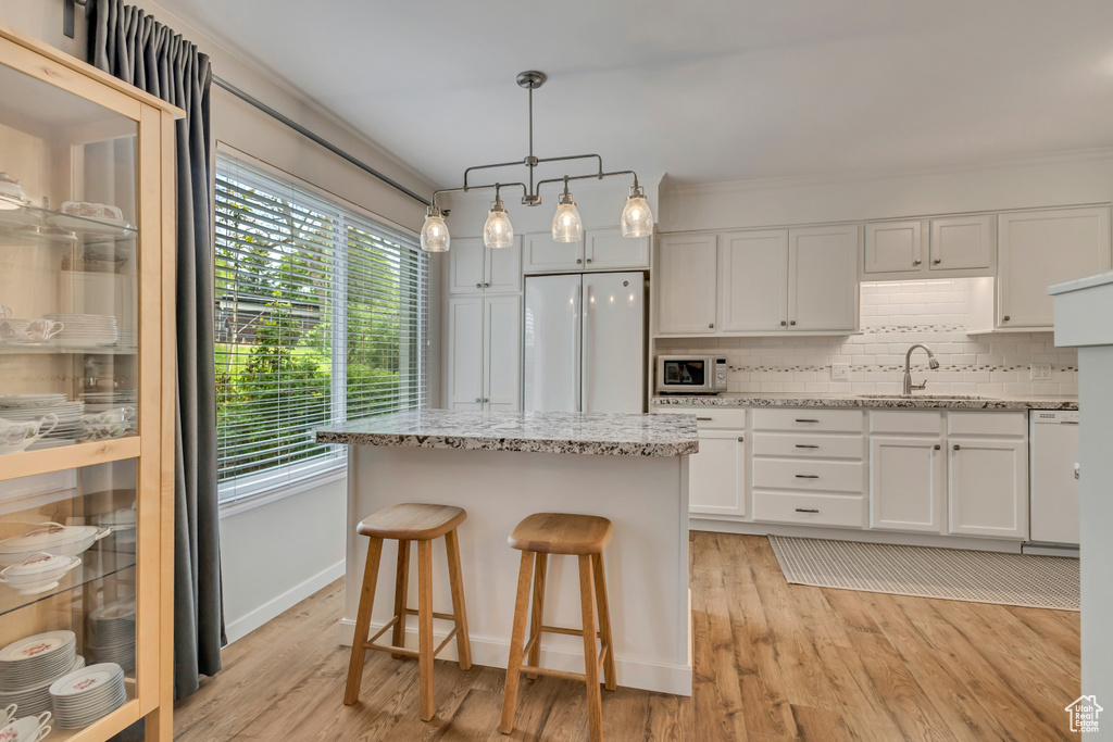 Kitchen with white appliances, a sink, white cabinetry, decorative backsplash, and a kitchen island