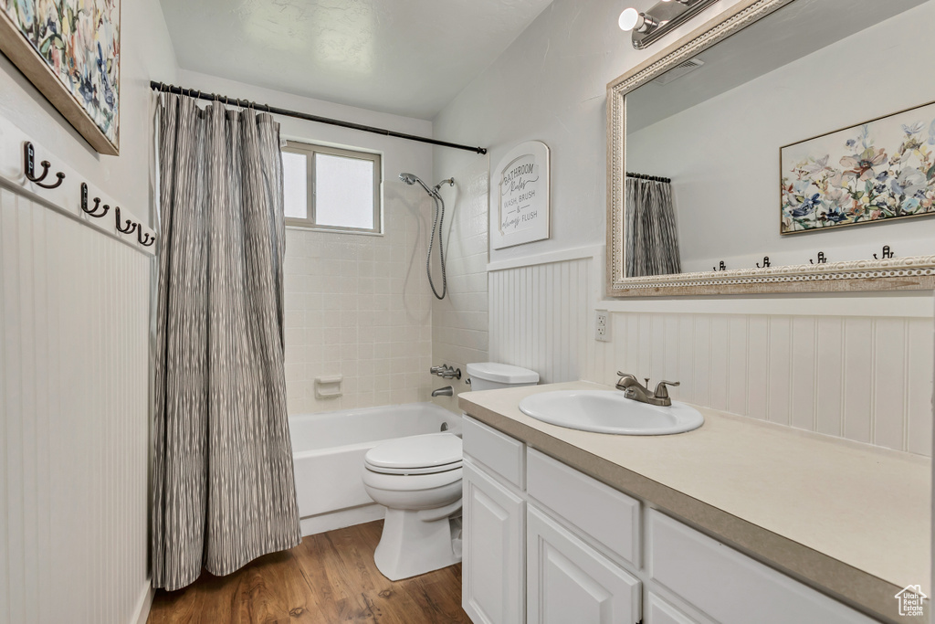 Bathroom with toilet, wood finished floors, a wainscoted wall, vanity, and shower / bathtub combination with curtain