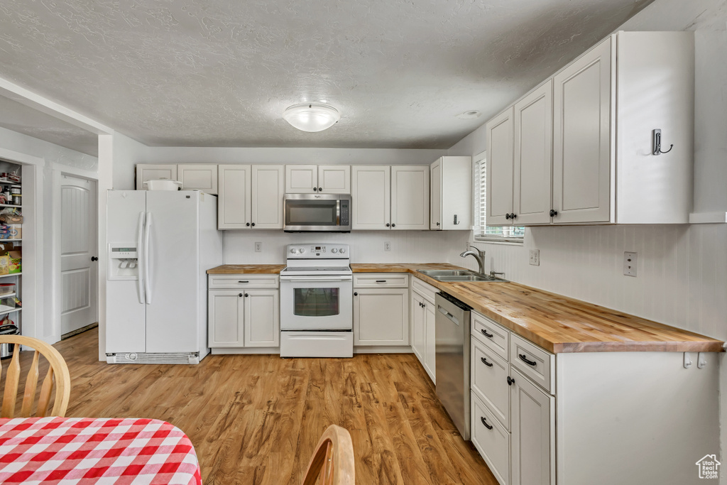 Kitchen with appliances with stainless steel finishes, butcher block countertops, a sink, light wood-type flooring, and white cabinets