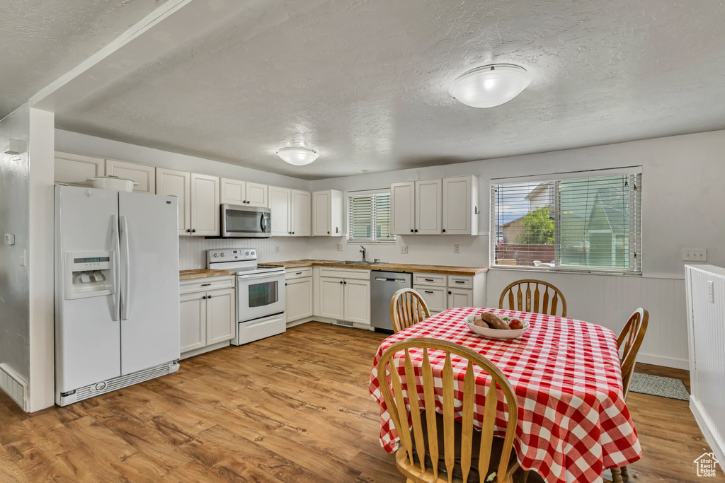 Kitchen with appliances with stainless steel finishes, a textured ceiling, light wood finished floors, a wainscoted wall, and a sink
