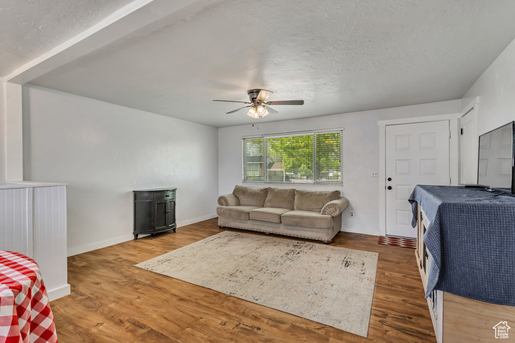 Living area with ceiling fan, wood finished floors, baseboards, and a textured ceiling