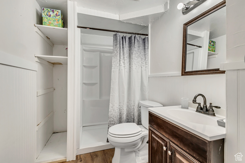 Bathroom featuring wood finished floors, a shower stall, vanity, toilet, and wainscoting