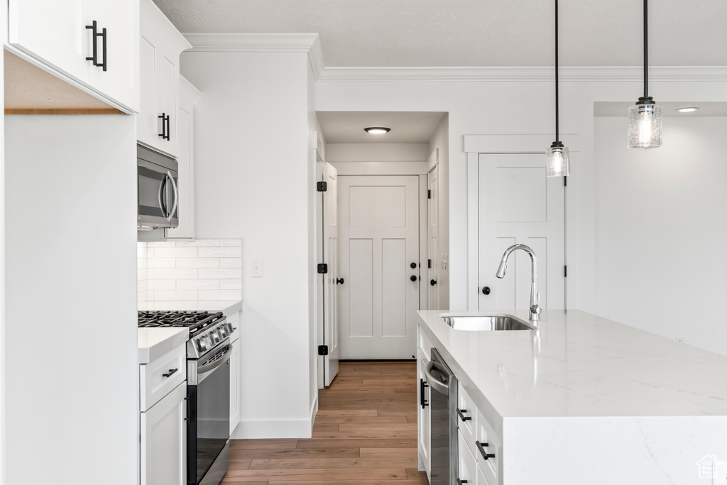 Kitchen featuring stainless steel appliances, a sink, ornamental molding, light wood-style floors, and white cabinetry