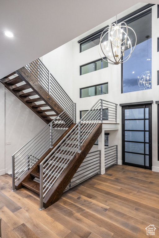 Stairs with a chandelier, wood finished floors, baseboards, and a high ceiling