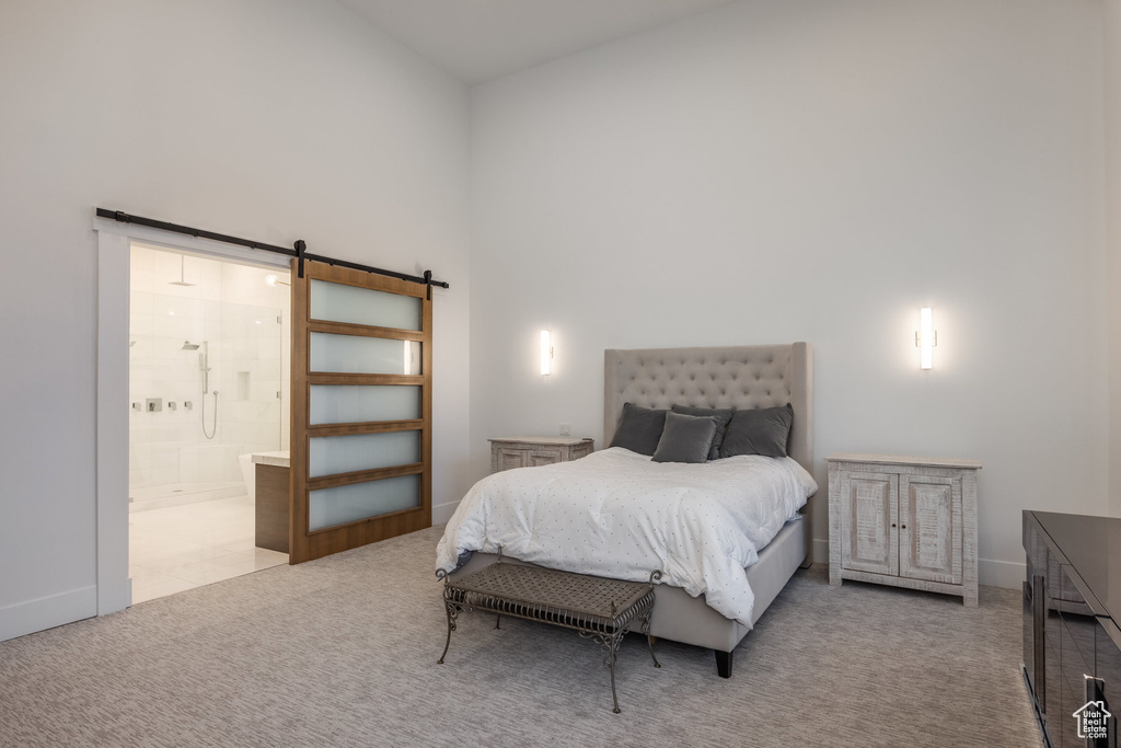Bedroom with a barn door, carpet flooring, high vaulted ceiling, baseboards, and ensuite bathroom