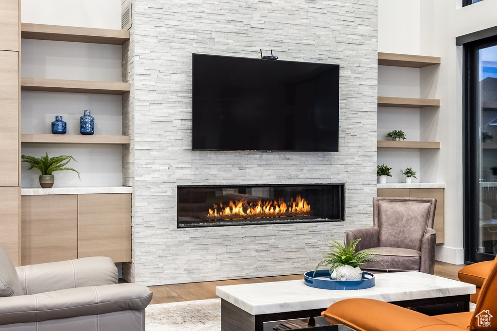 Living room with wood finished floors, a stone fireplace, and built in shelves