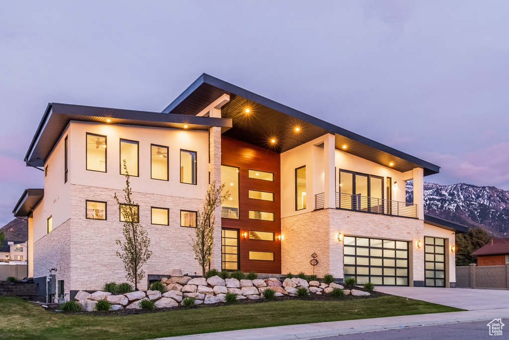 Modern home with stone siding, a garage, a mountain view, stucco siding, and driveway