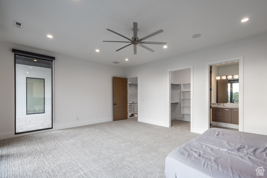 Bedroom featuring light colored carpet, a walk in closet, recessed lighting, ensuite bath, and baseboards