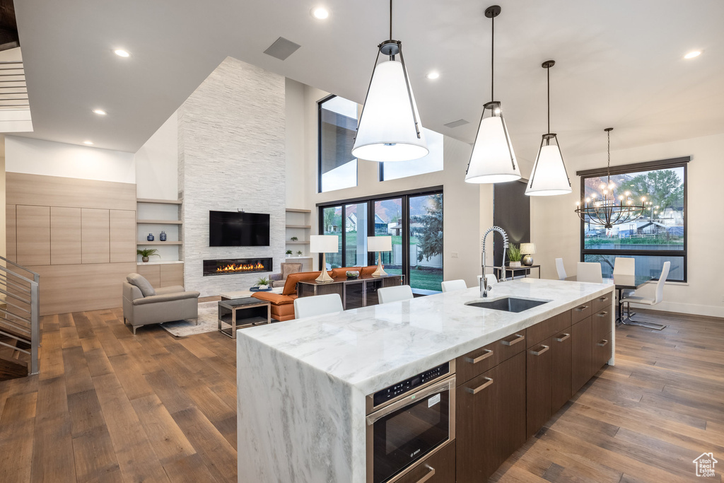 Kitchen with a sink, dark brown cabinetry, a large island, a stone fireplace, and dark wood finished floors