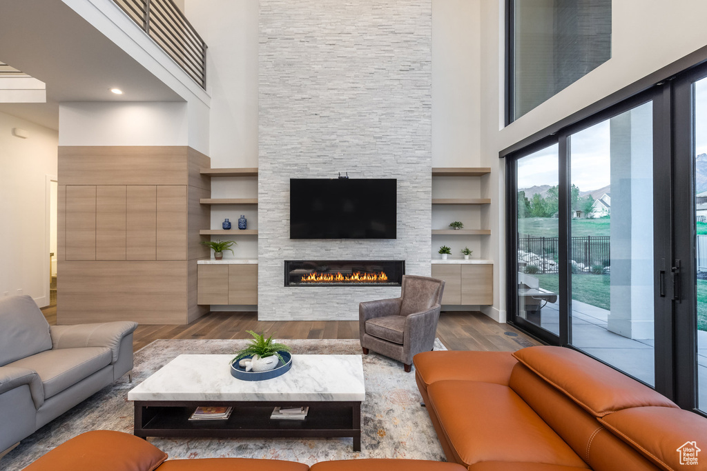 Living room featuring dark wood-style flooring, a high ceiling, and a stone fireplace