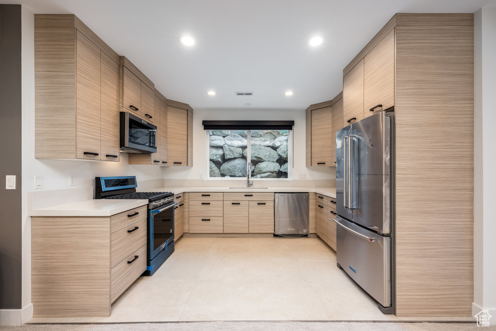 Kitchen with appliances with stainless steel finishes, light brown cabinets, light countertops, a sink, and recessed lighting