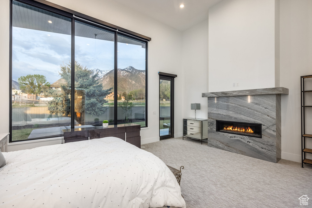Carpeted bedroom featuring a warm lit fireplace, baseboards, access to exterior, and a mountain view