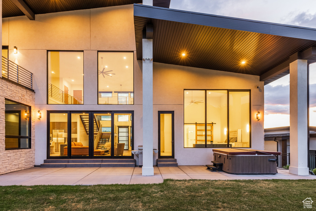 Back of house with a hot tub, a patio area, and stucco siding