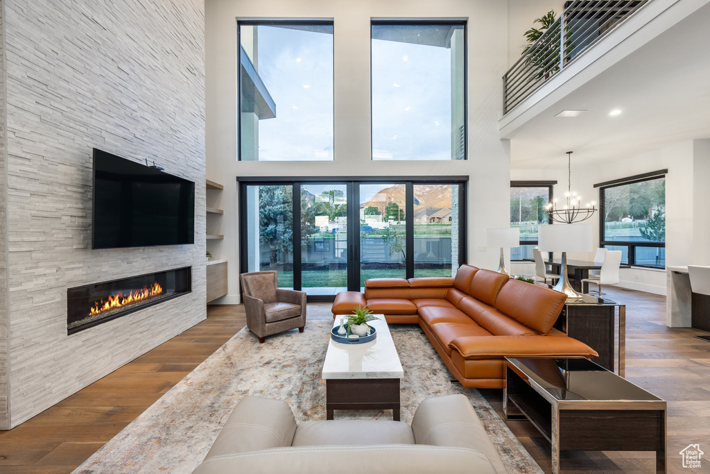 Living room featuring wood finished floors, a stone fireplace, a high ceiling, and a chandelier