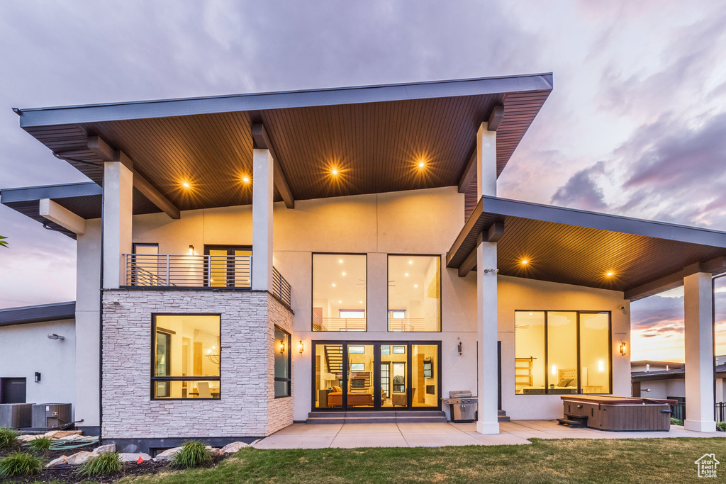 Rear view of house with a hot tub, stone siding, stucco siding, central AC, and a patio