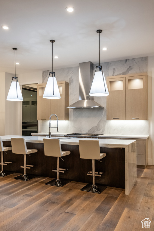 Kitchen with wall chimney range hood, modern cabinets, wood finished floors, light countertops, and light brown cabinets