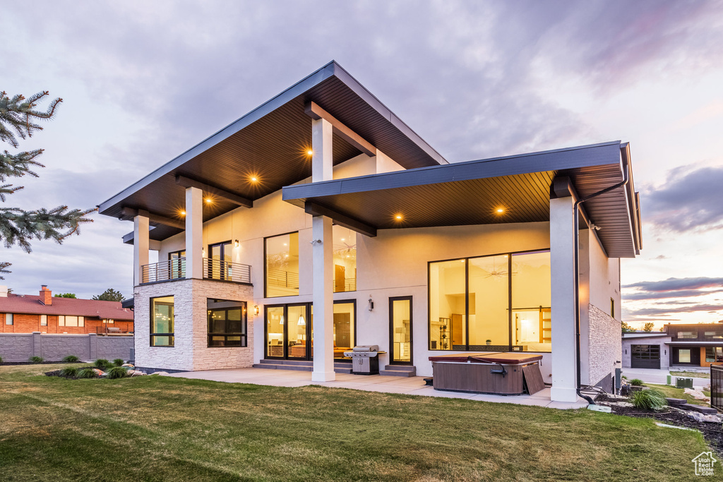 Back of house with a hot tub, a balcony, a patio, and stucco siding