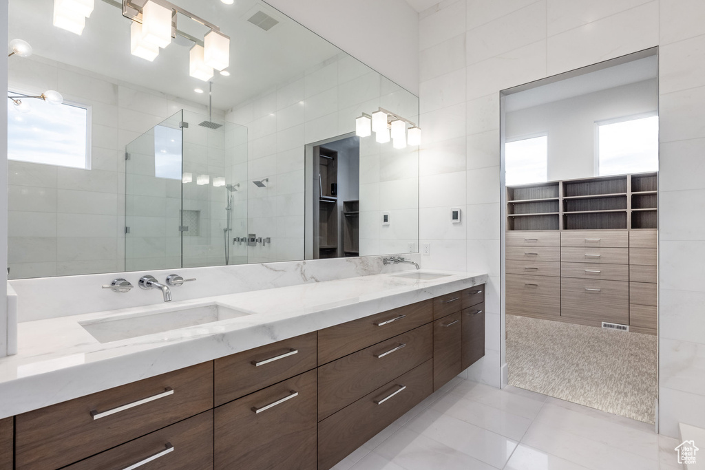 Full bathroom with a shower stall, tile patterned floors, tile walls, double vanity, and a walk in closet