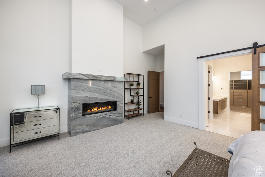 Carpeted bedroom featuring a high end fireplace, baseboards, a high ceiling, a barn door, and ensuite bathroom
