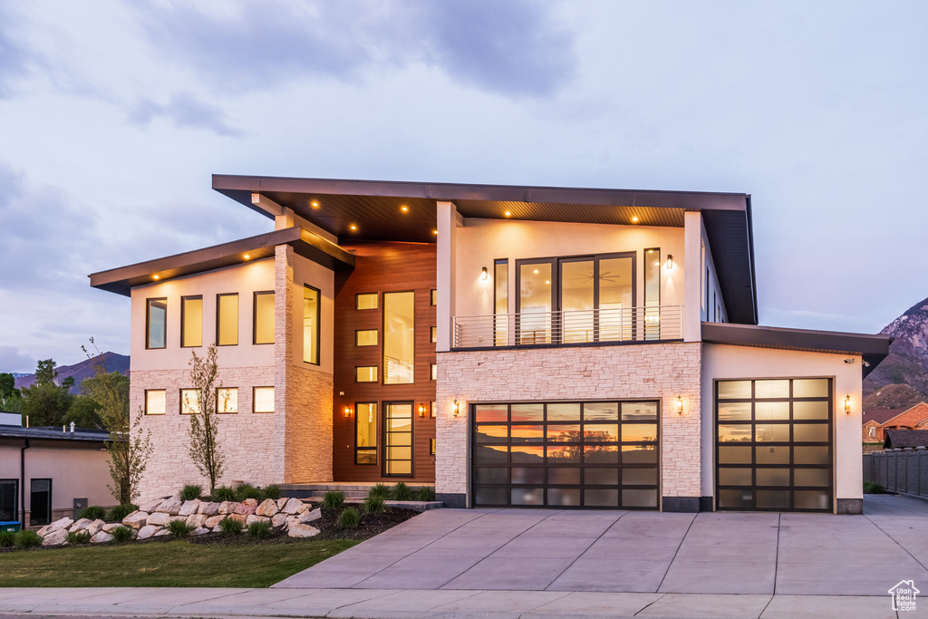 Modern home with driveway, a balcony, stone siding, and stucco siding