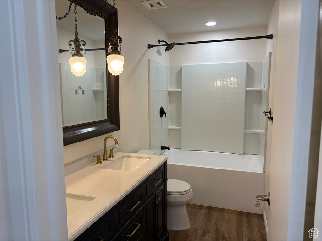 Full bathroom with wood finished floors, toilet, double vanity, and washtub / shower combination