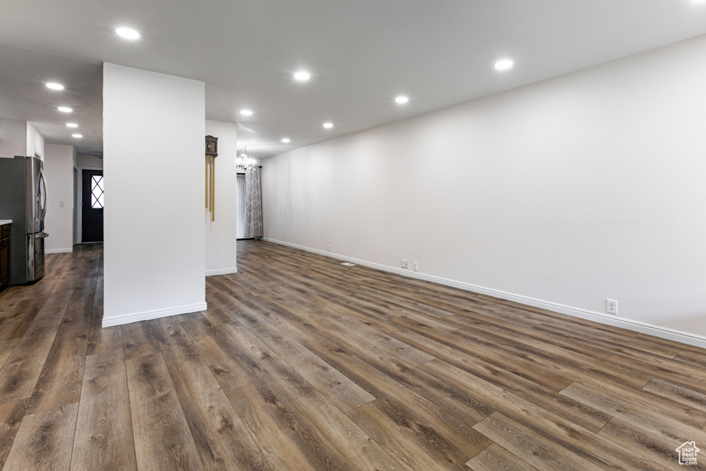 Unfurnished living room featuring dark wood finished floors, baseboards, recessed lighting, and a chandelier