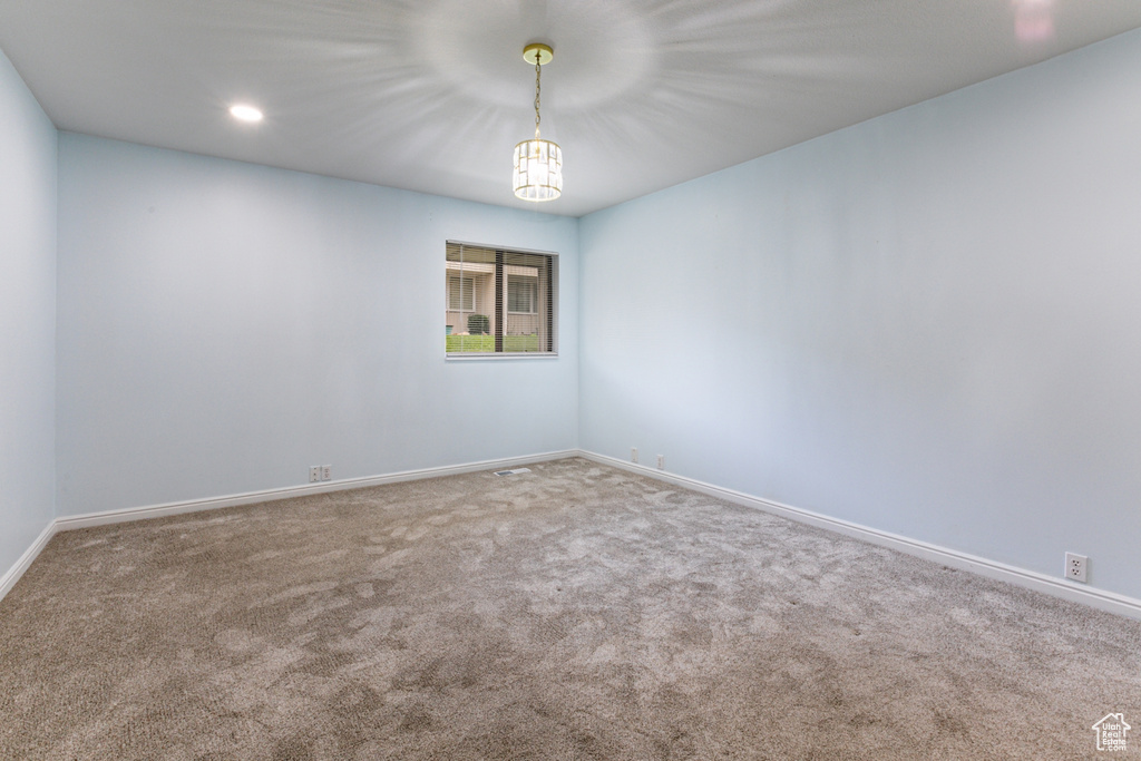 Carpeted empty room with baseboards, recessed lighting, and a chandelier