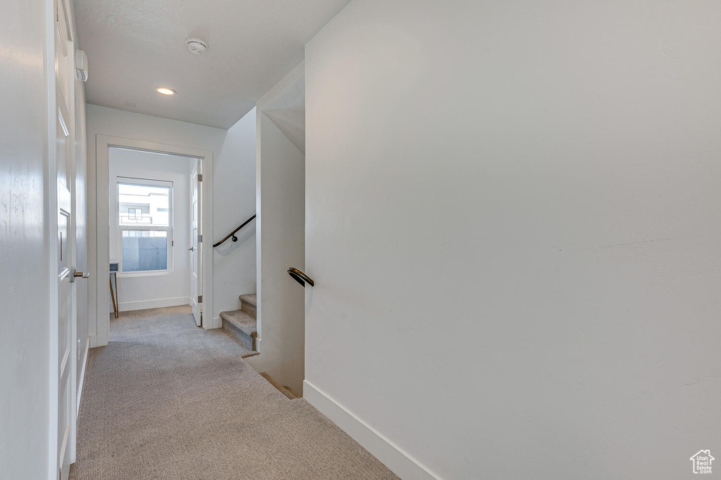 Hallway featuring light carpet, baseboards, recessed lighting, and stairway