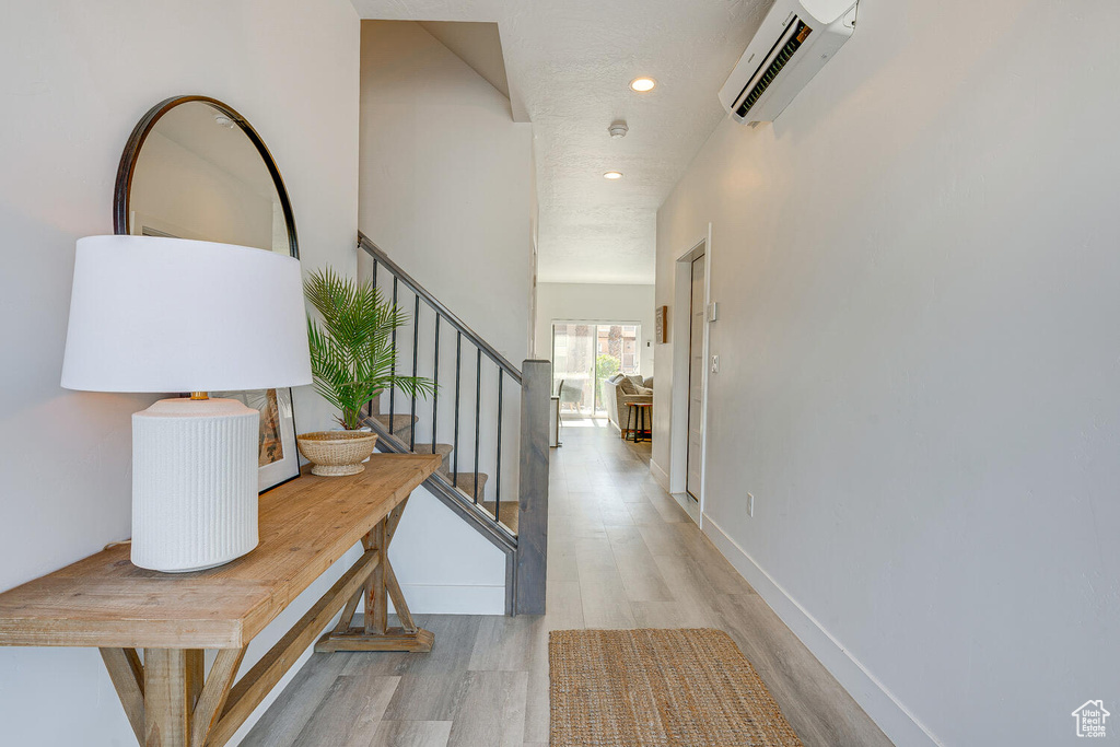 Hall featuring light wood-style floors, a wall mounted AC, recessed lighting, stairs, and baseboards