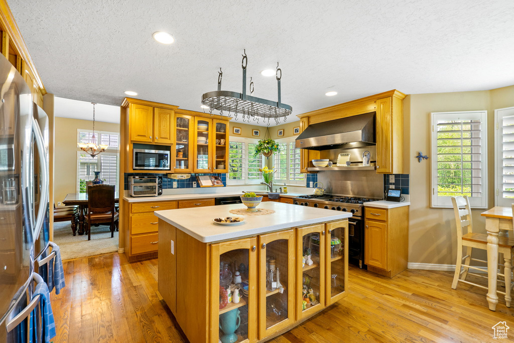 Kitchen with wall chimney exhaust hood, stainless steel appliances, light countertops, light wood-type flooring, and a textured ceiling