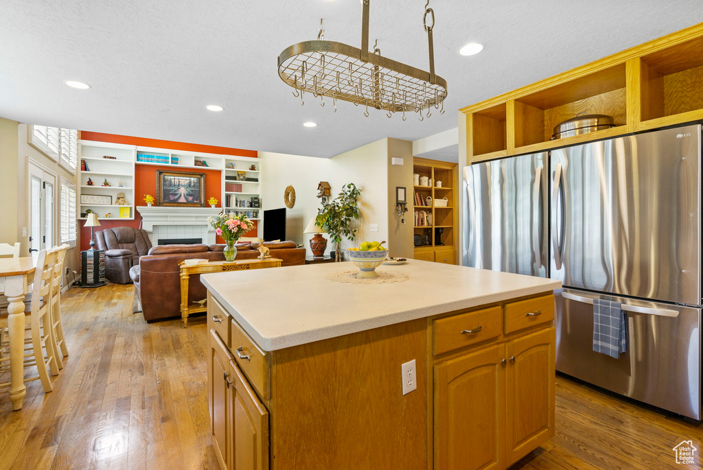 Kitchen with open shelves, freestanding refrigerator, light wood-style flooring, a kitchen island, and light countertops