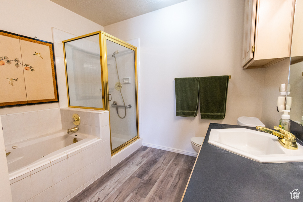 Full bath featuring toilet, wood finished floors, a stall shower, a bath, and baseboards