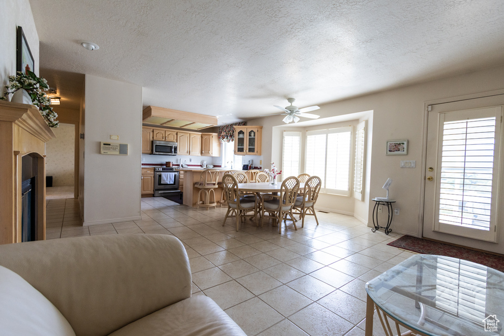Dining space with light tile patterned floors, baseboards, ceiling fan, a textured ceiling, and a fireplace