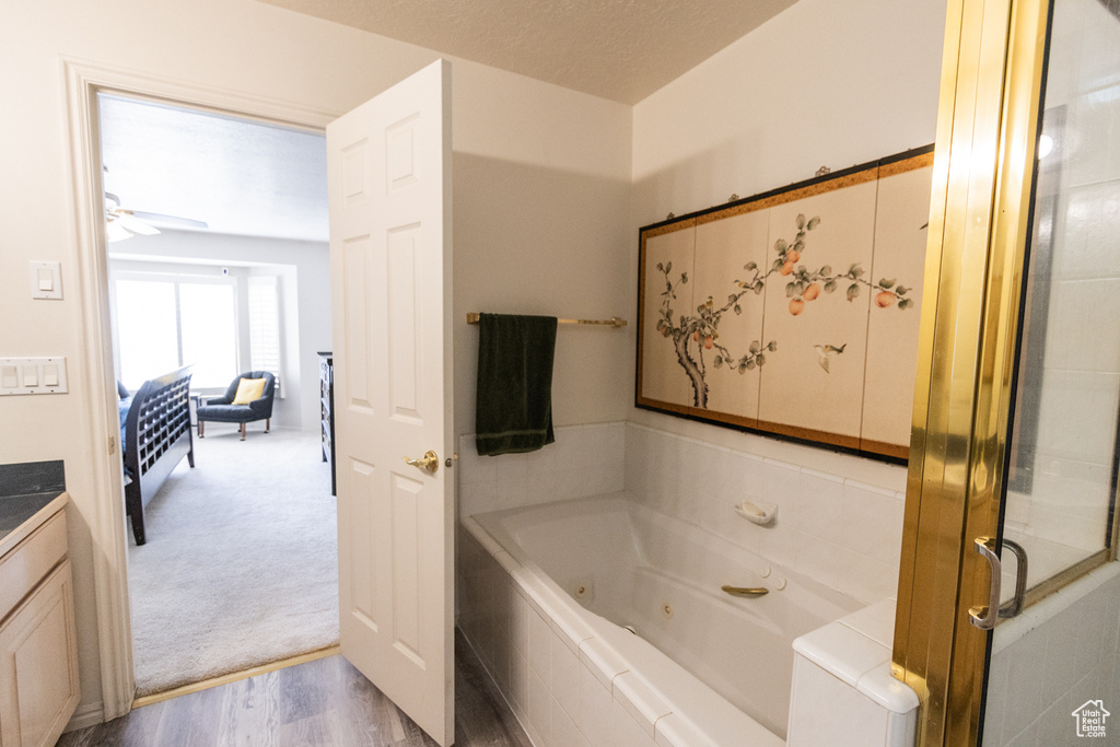 Bathroom featuring a tub with jets, ceiling fan, wood finished floors, and vanity