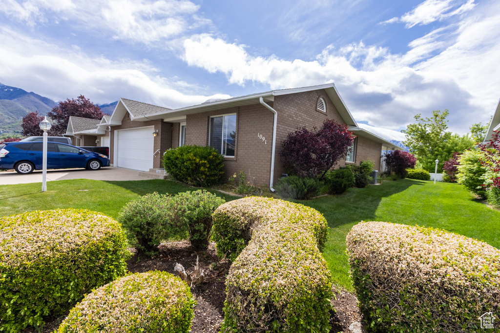 View of front facade featuring an attached garage, brick siding, a front yard, a mountain view, and driveway