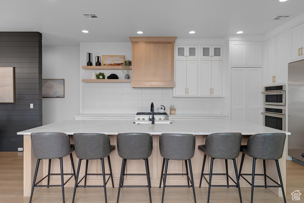 Kitchen featuring a sink, stainless steel appliances, decorative backsplash, white cabinets, and light wood-style flooring