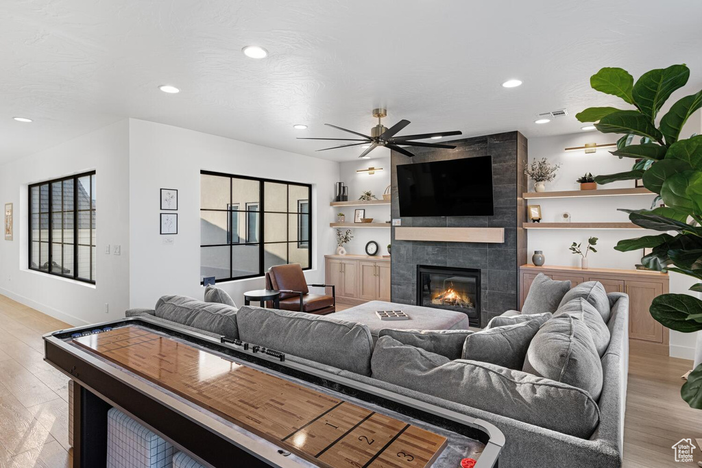 Living room with light wood-style flooring, a ceiling fan, a tiled fireplace, recessed lighting, and baseboards