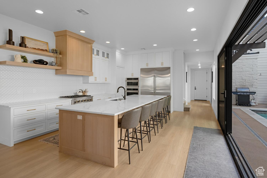 Kitchen with light wood-style floors, a sink, stainless steel appliances, tasteful backsplash, and a kitchen bar