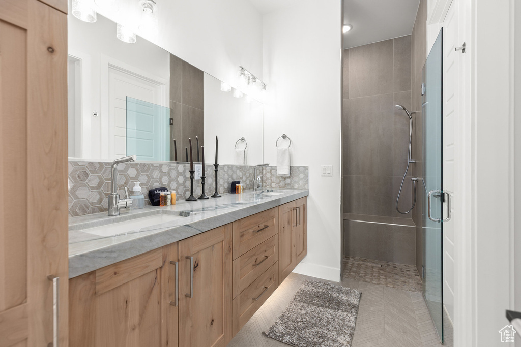 Full bathroom featuring a tile shower, decorative backsplash, double vanity, tile patterned flooring, and baseboards