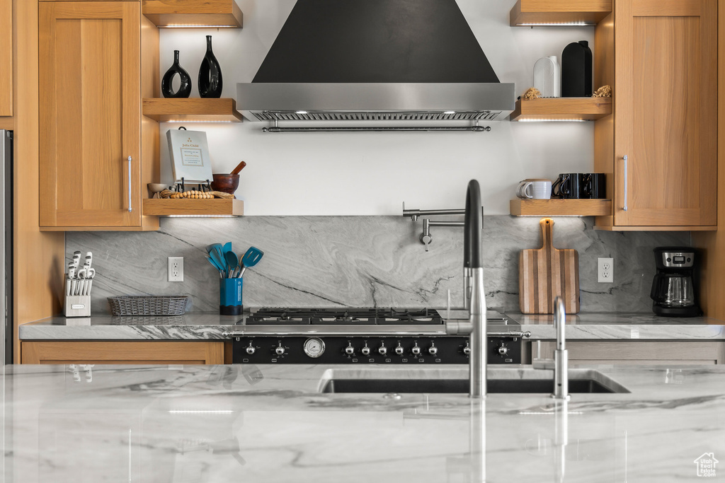 Kitchen featuring open shelves, wall chimney range hood, backsplash, and a sink