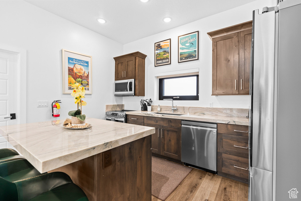 Kitchen featuring appliances with stainless steel finishes, a sink, a kitchen bar, light stone countertops, and light wood-style flooring