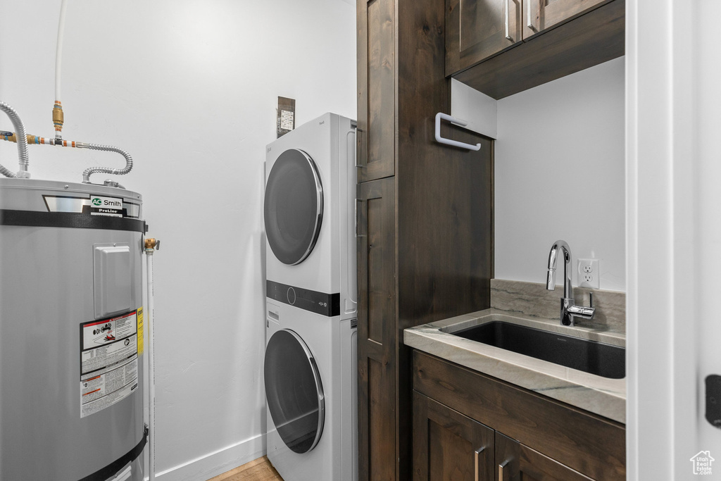 Washroom featuring electric water heater, estacked washer and dryer, cabinet space, and baseboards