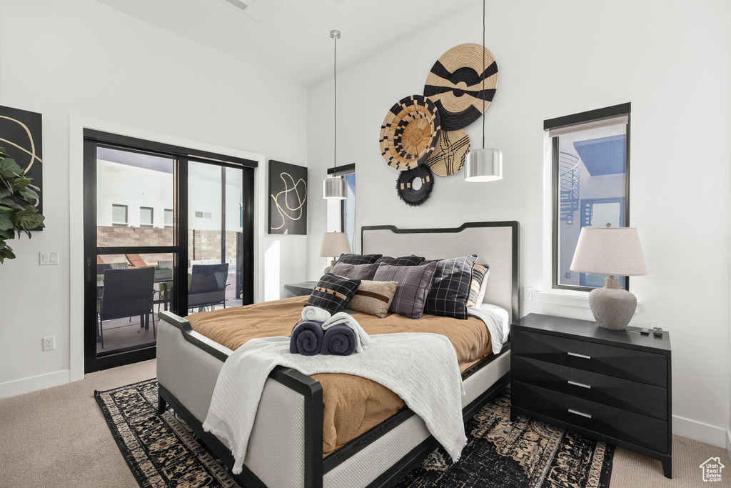 Bedroom featuring light colored carpet, access to outside, multiple windows, and a towering ceiling